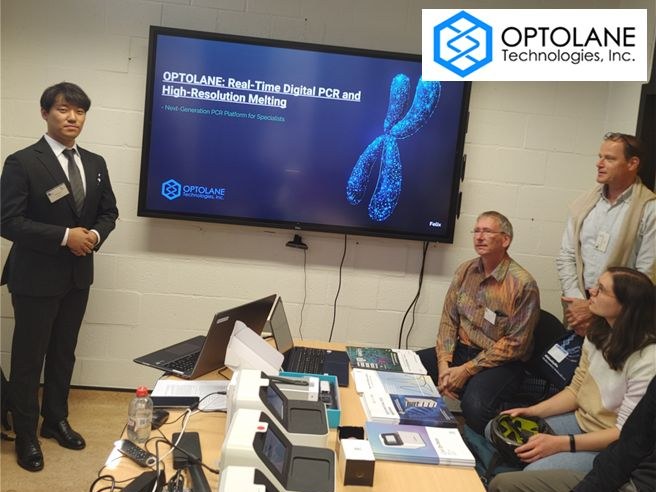 The same session from the front: Jinwoo Seol standing next to the OPTOLANE title slide, three listeners at the right and LOAA instruments in the foreground; an OPTOLANE logo from the organizers' collage overlaps the top-right corner