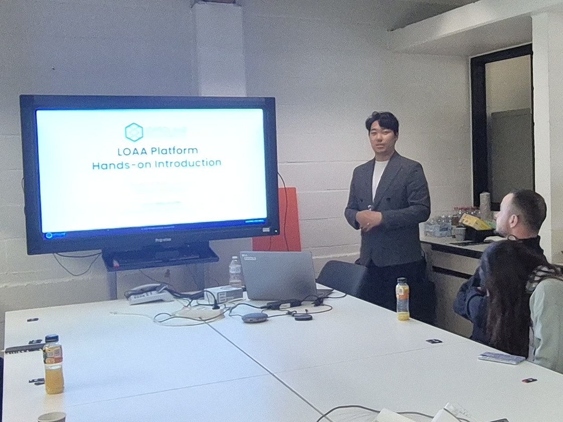 Jinwoo Seol standing beside a display that reads “LOAA Platform Hands-on Introduction,” speaking to seated attendees